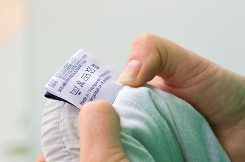 Close-up of person reading the clothing label showing washing instructions at home.
